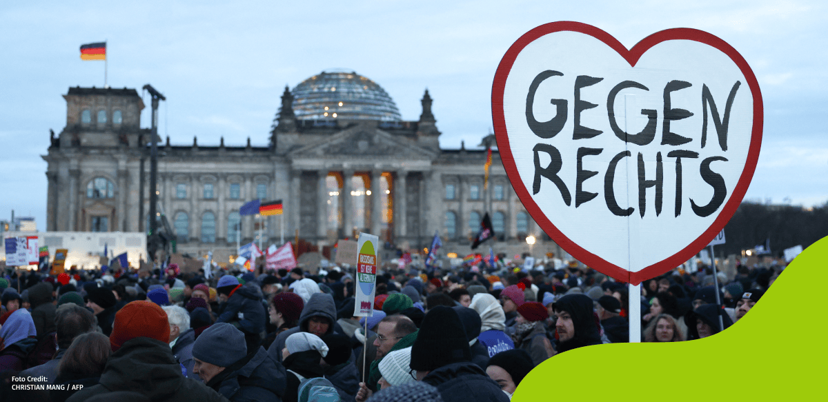 Wir sehen eine große Masse an Menschen mit Plakaten und Flaggen bei der Demonstration am 21. Januar vor dem Bundestag. Rechts auf dem Bild sehen wir ein ein sehr großes herzförmiges Plakat mit rotem Rand, auf dem steht “Gegen Rechts”.