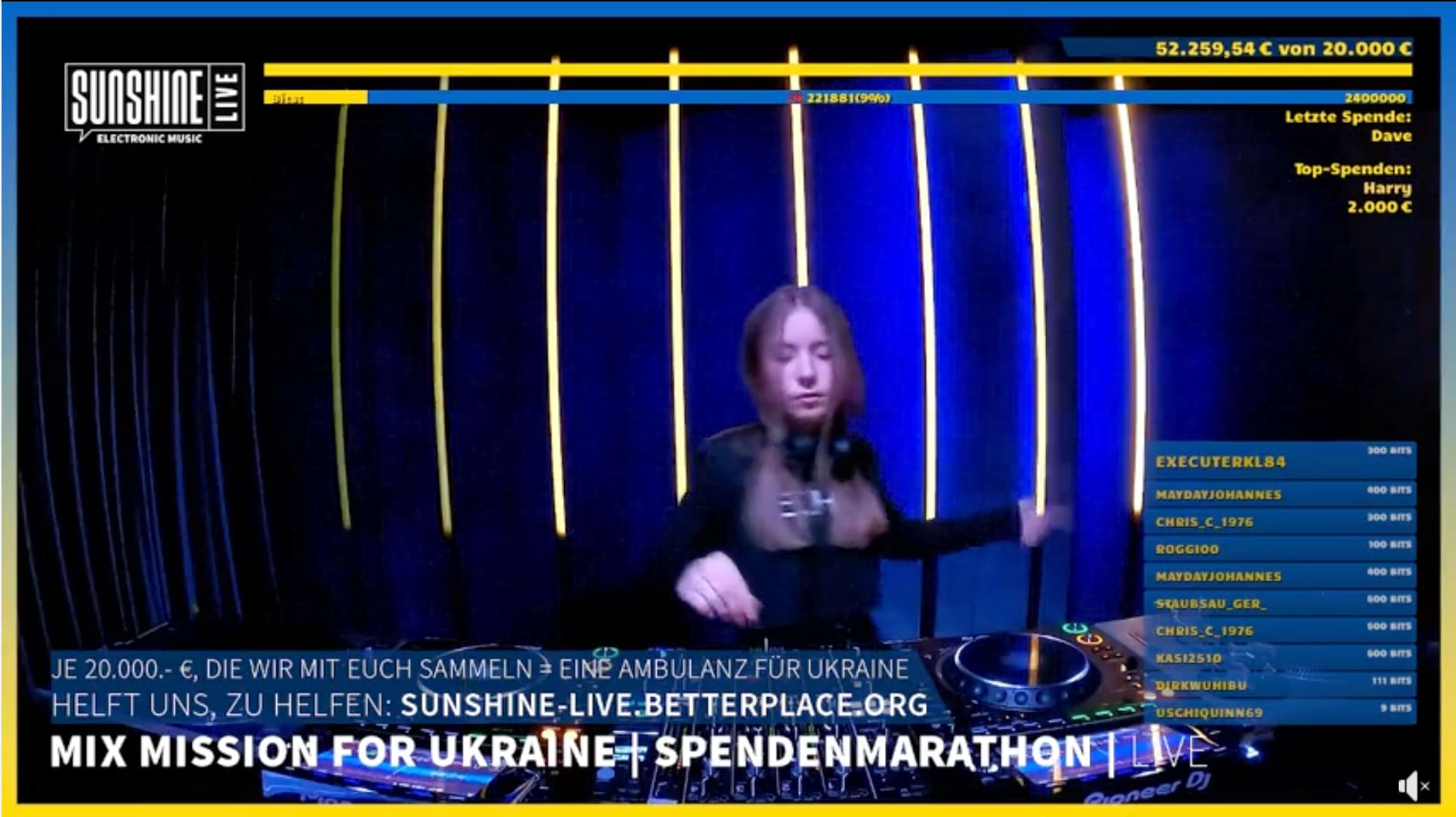 Wir sehen einen Screenshot vom DJ-Mix Spendenmarathon auf SUNSHINE LIVE. Eine junge weiße Frau mit glatten blonden langen Haaren steht schwarz gekleidet und mit Kopfhörern um den Hals gehängt hinter dem DJ-Controller. Oben im Screen sehen wir in gelb auf blau den Spendenstand auf dem Spendenbalken: 52.259,54 € von 20.000 €. Darunter "Letzte Spende: Dave" und "Top-Spenden: Harry 2.000 €